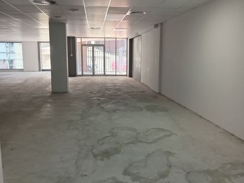 A spacious, open-plan commercial interior featuring a suspended ceiling, recessed lighting, and large windows, currently presented as a blank canvas with unfinished flooring.