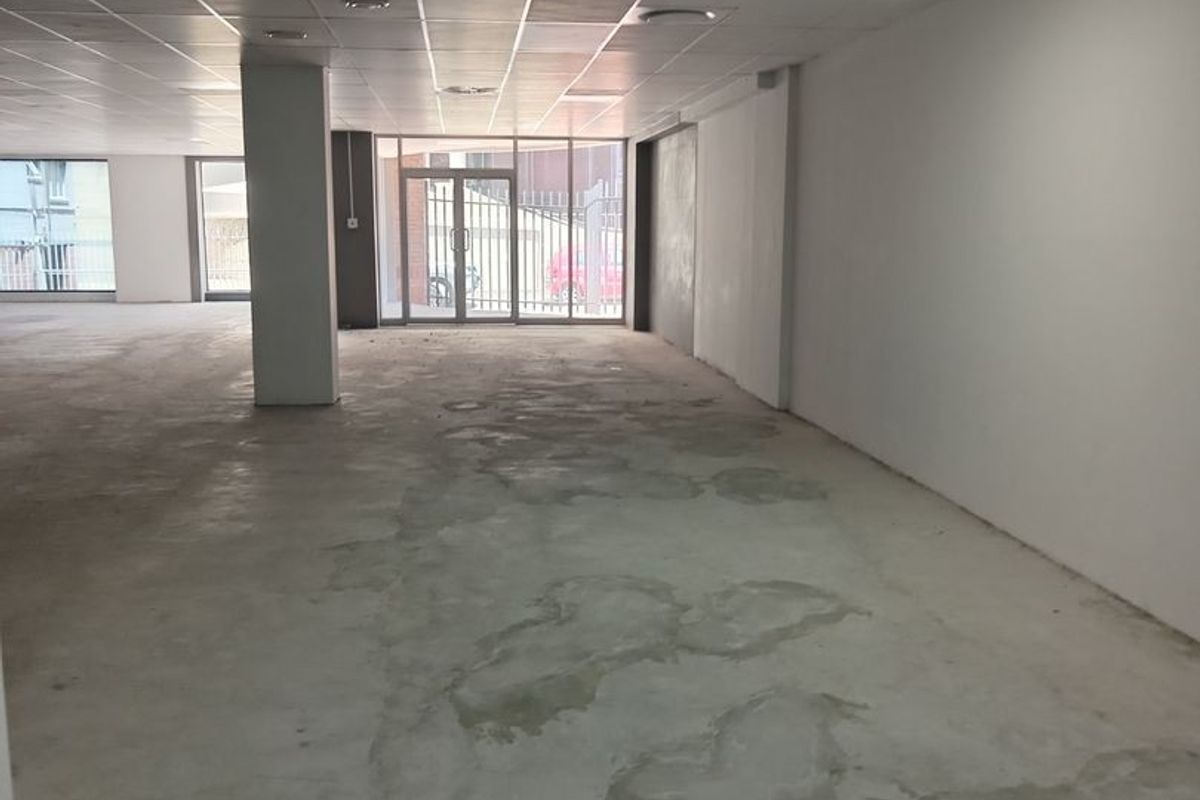 A spacious, open-plan commercial interior featuring a suspended ceiling, recessed lighting, and large windows, currently presented as a blank canvas with unfinished flooring.