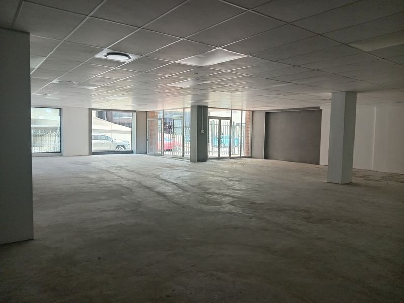 Spacious open-plan commercial unit featuring a suspended ceiling, recessed lighting, concrete flooring, and large glass storefront windows providing ample natural light.