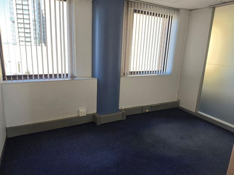 Empty commercial office space featuring blue carpet flooring, a structural column, vertical blinds, and a frosted glass partition wall.