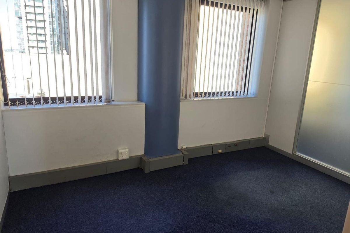 Empty commercial office space featuring blue carpet flooring, a structural column, vertical blinds, and a frosted glass partition wall.