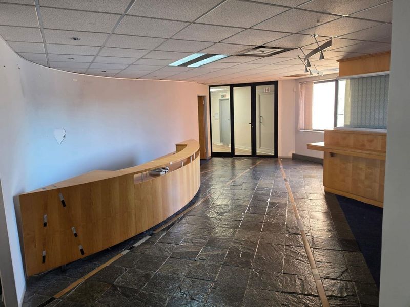 Spacious commercial reception area featuring a curved built-in desk, stone tile flooring, and glass partition doors, offering a professional entry point for clients.