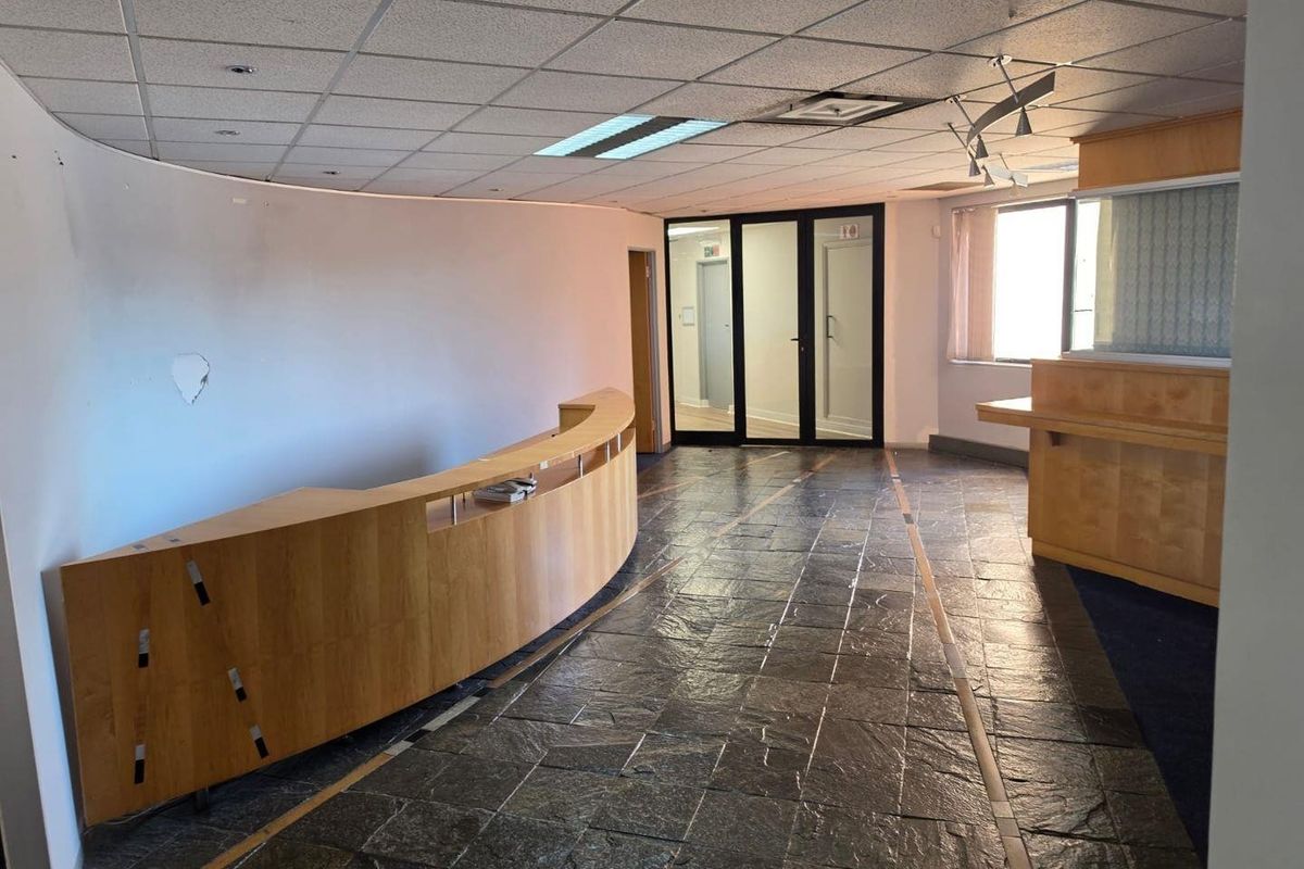 Spacious commercial reception area featuring a curved built-in desk, stone tile flooring, and glass partition doors, offering a professional entry point for clients.