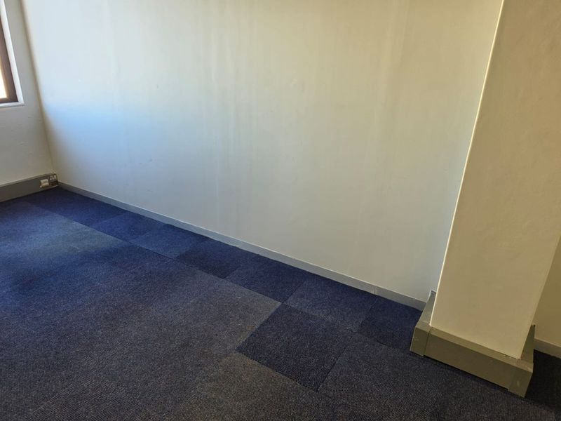 An empty office space featuring blue carpet tiles, a structural column, and plain walls, suitable for a professional workspace setup.