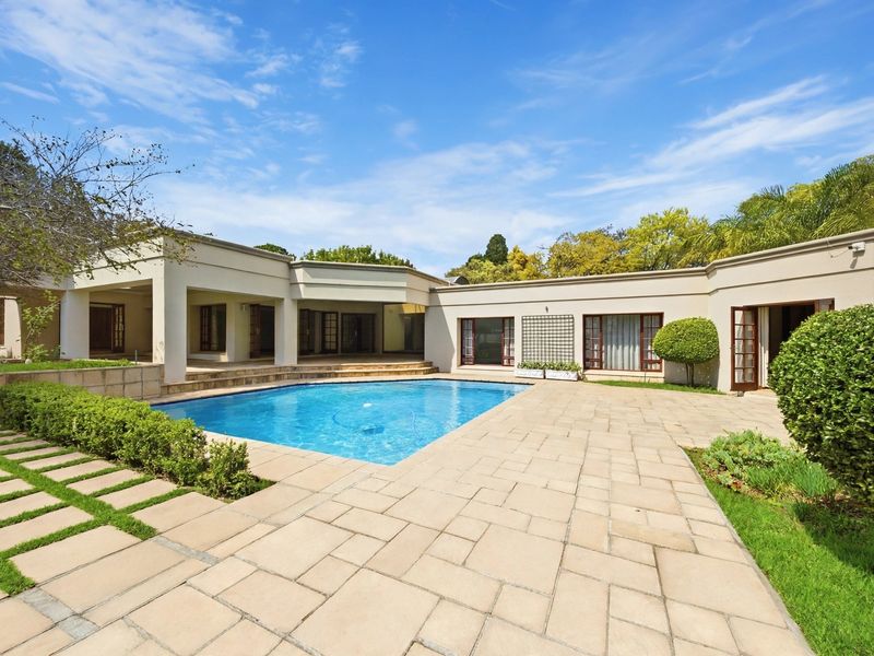 Spacious rear outdoor area featuring a swimming pool, extensive paved patio, and covered veranda with direct access to the home through multiple french doors.