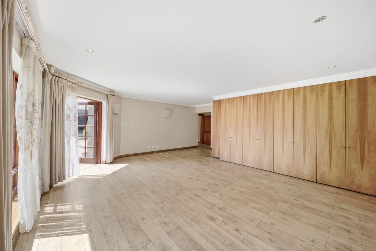 Spacious bedroom featuring extensive built-in wooden cupboards, light laminate flooring, recessed downlighting, and direct access to the exterior through classic french doors.