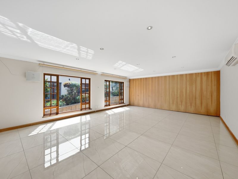 Spacious, light-filled living area featuring polished porcelain floor tiles, extensive built-in wooden cabinetry, and split-system air conditioning.