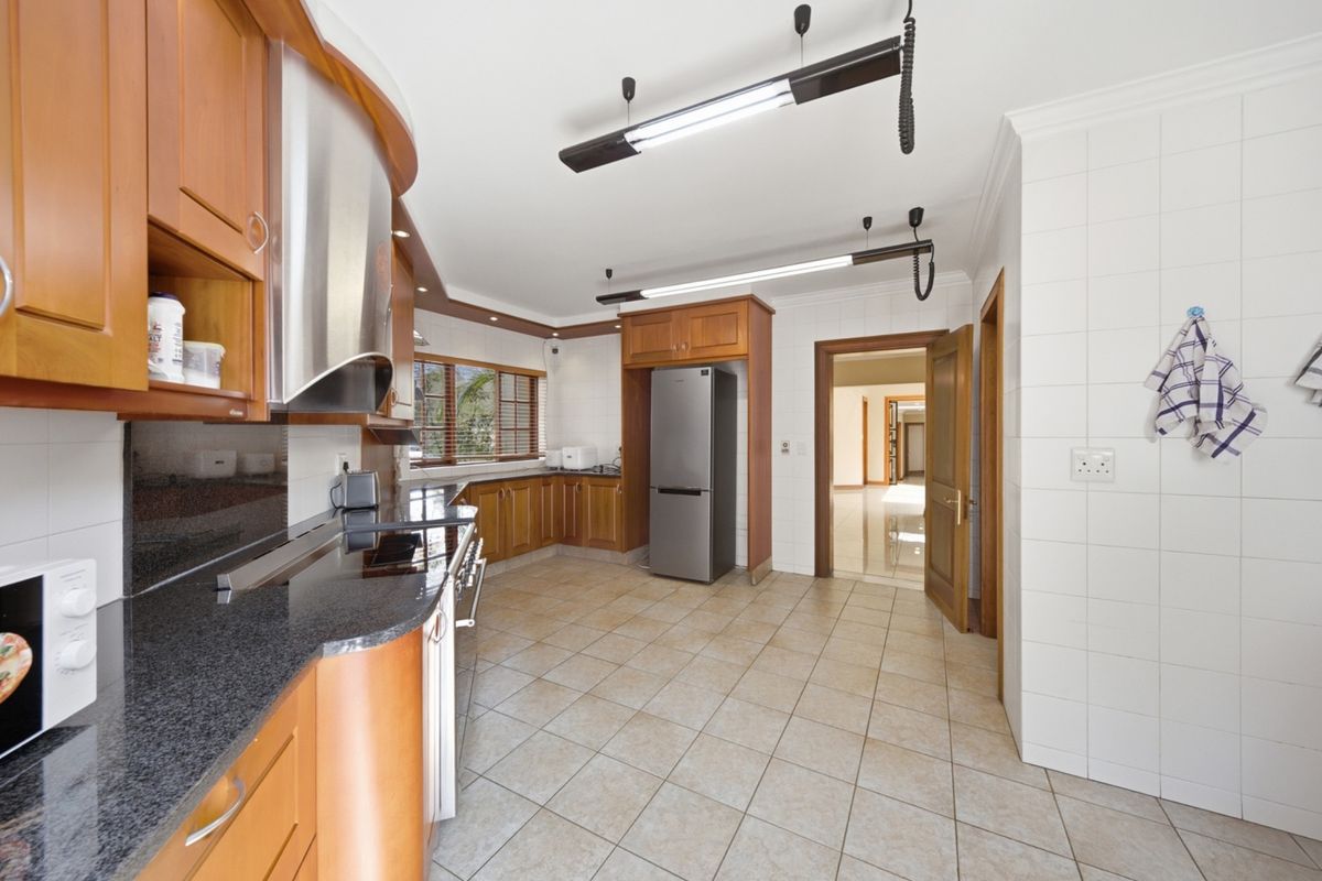 A spacious kitchen featuring wooden cabinetry, granite countertops, tiled splashbacks, and ceramic tile flooring, offering a functional layout with ample storage space.