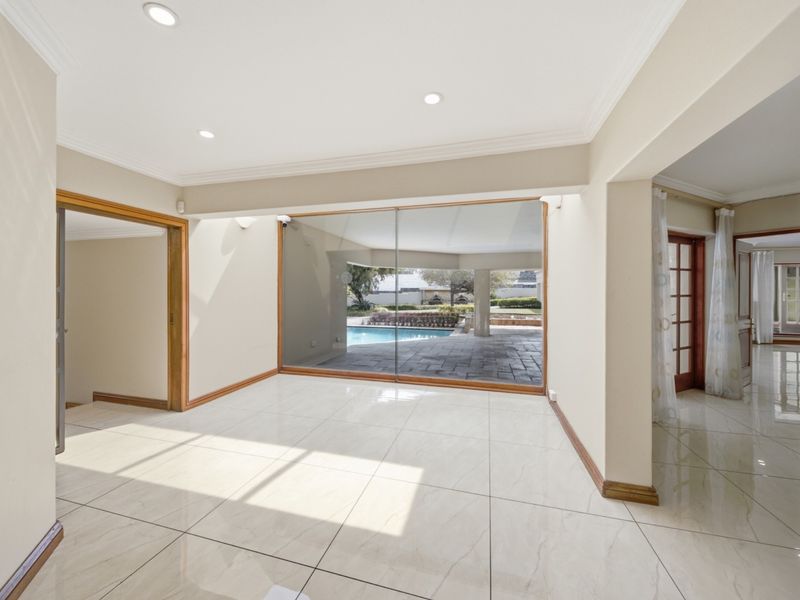 A bright, empty living area featuring large sliding glass doors that provide a seamless transition to the outdoor patio and pool area.