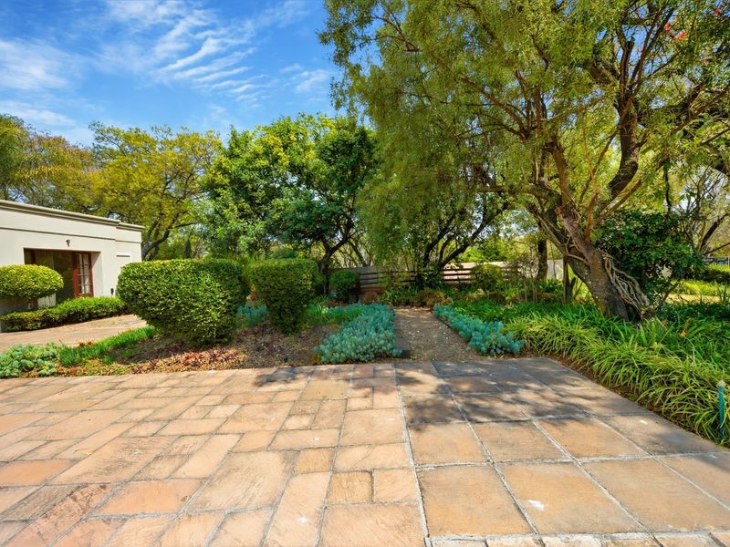A well-maintained garden area featuring a paved patio, established trees, and a stone pathway leading through landscaped beds.