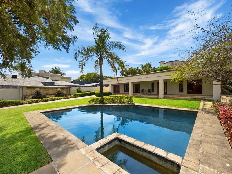 A well-maintained outdoor area featuring a swimming pool, stone water feature, covered patio, and landscaped garden.