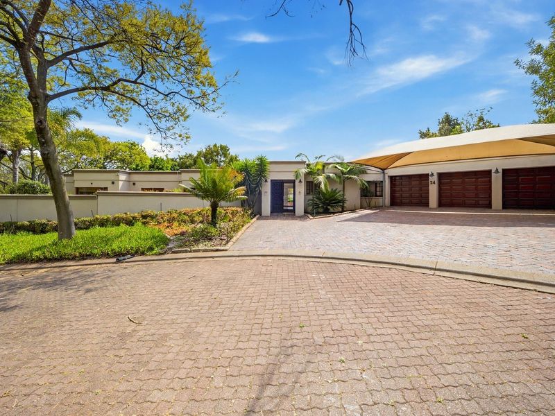 Front exterior view of the property featuring a paved driveway, double garage with shade sail, and well-maintained landscaped garden.