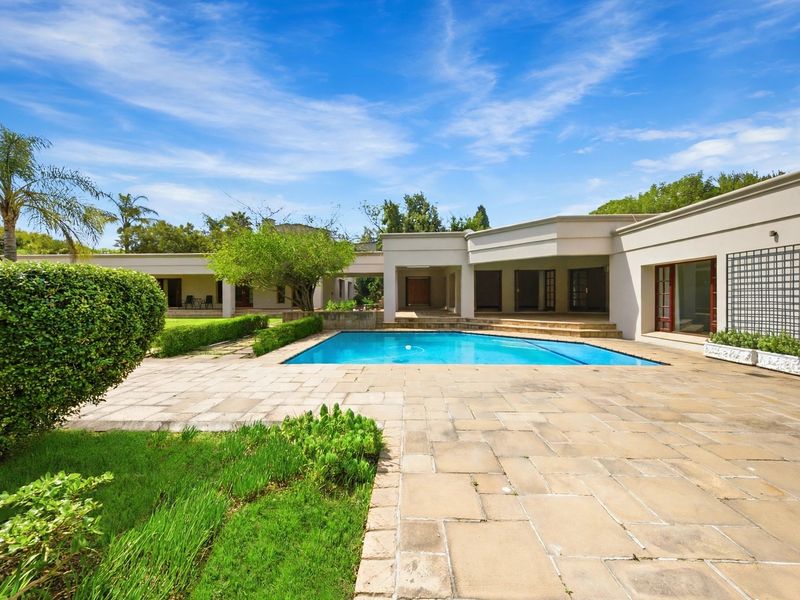 Spacious outdoor entertainment area featuring a swimming pool, expansive stone-paved patio, and a covered veranda overlooking the landscaped garden.