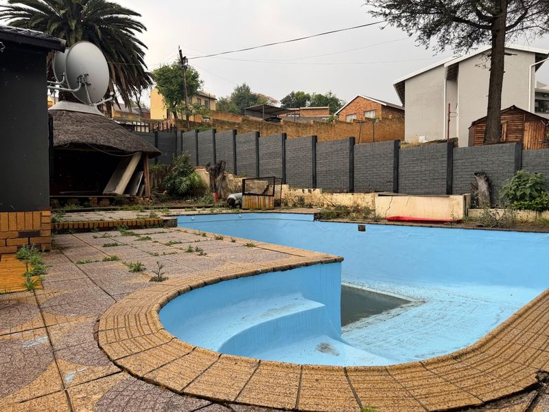 Outdoor pool area featuring a swimming pool, paved surround, and a thatched lapa, currently requiring significant maintenance and restoration.