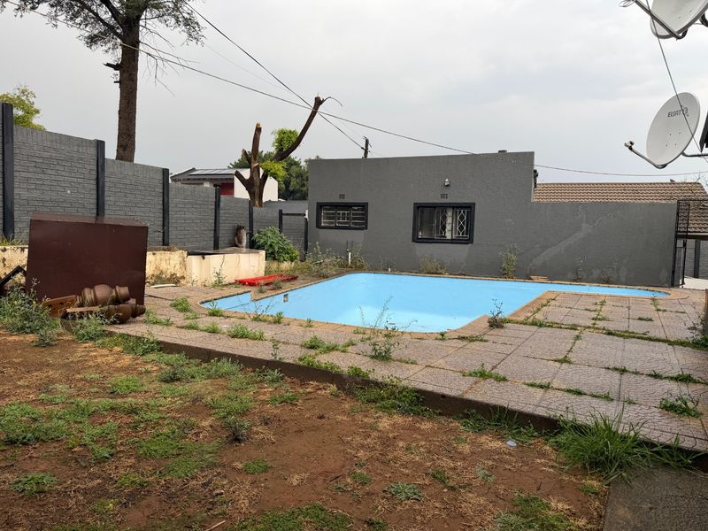 Outdoor pool area featuring a swimming pool with paved surround and perimeter walling, currently requiring landscaping and maintenance to restore its appeal.