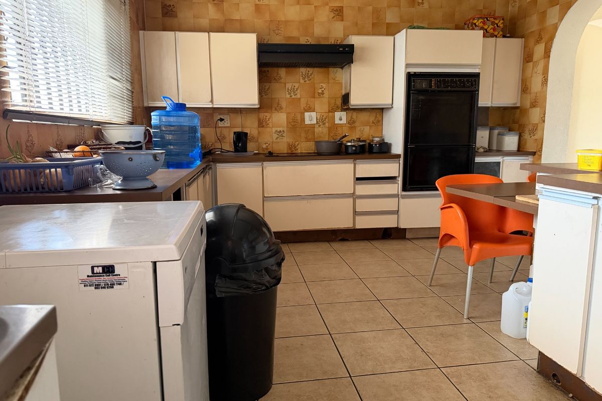 A dated kitchen featuring original cabinetry, built-in oven, extractor fan, and tiled flooring, offering significant potential for a modern renovation.