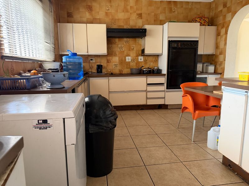 A dated kitchen featuring original cabinetry, built-in oven, extractor fan, and tiled flooring, offering significant potential for a modern renovation.