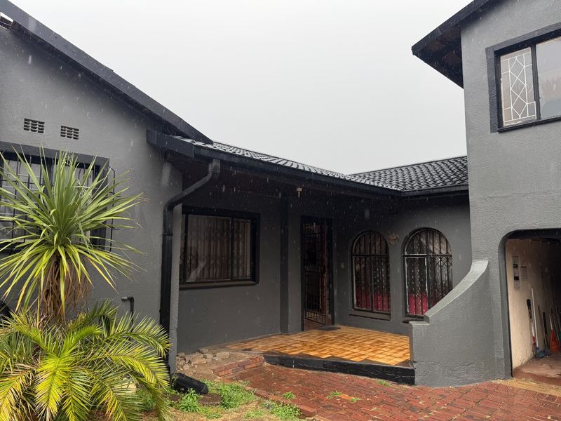 Front entrance area featuring a covered tiled patio, security bars on windows, and brick paved driveway access.