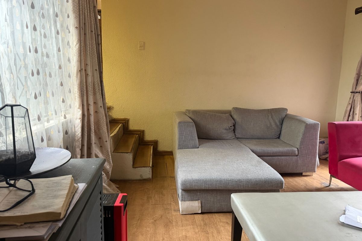 Living room area featuring laminate flooring and an internal staircase, requiring cosmetic updates to improve the overall aesthetic and condition of the space.