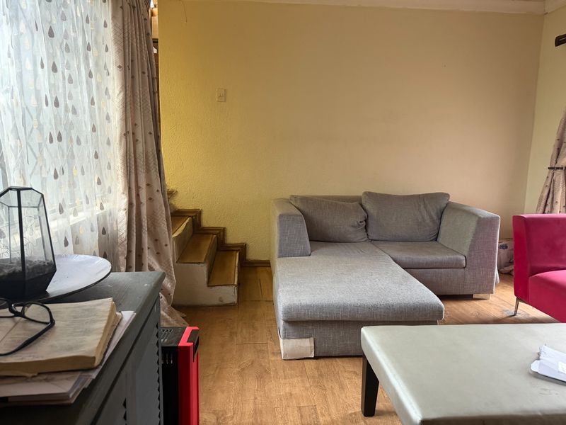 Living room area featuring laminate flooring and an internal staircase, requiring cosmetic updates to improve the overall aesthetic and condition of the space.