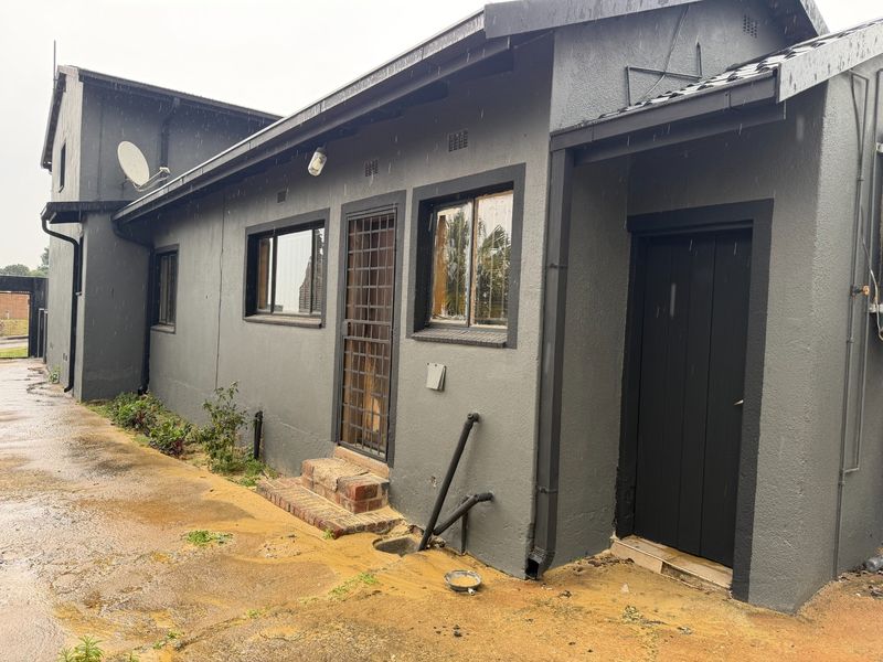 Rear exterior view of the house featuring dark grey painted walls, security gate, and exposed drainage pipes on a concrete paved area.