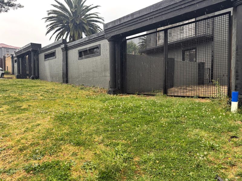 Front exterior view featuring a secure perimeter wall with decorative columns and a large metal security gate.