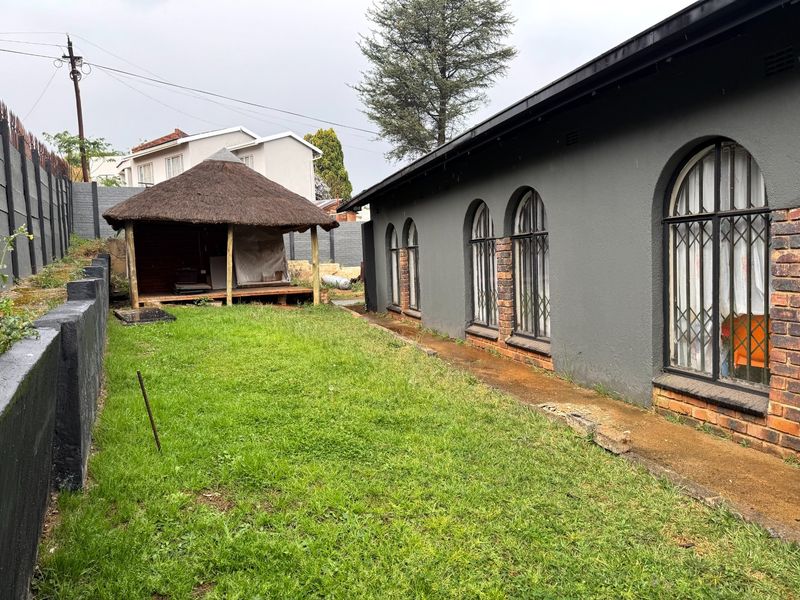 Rear garden area featuring a thatched lapa, concrete pathway, and arched windows along the side of the house with security bars.