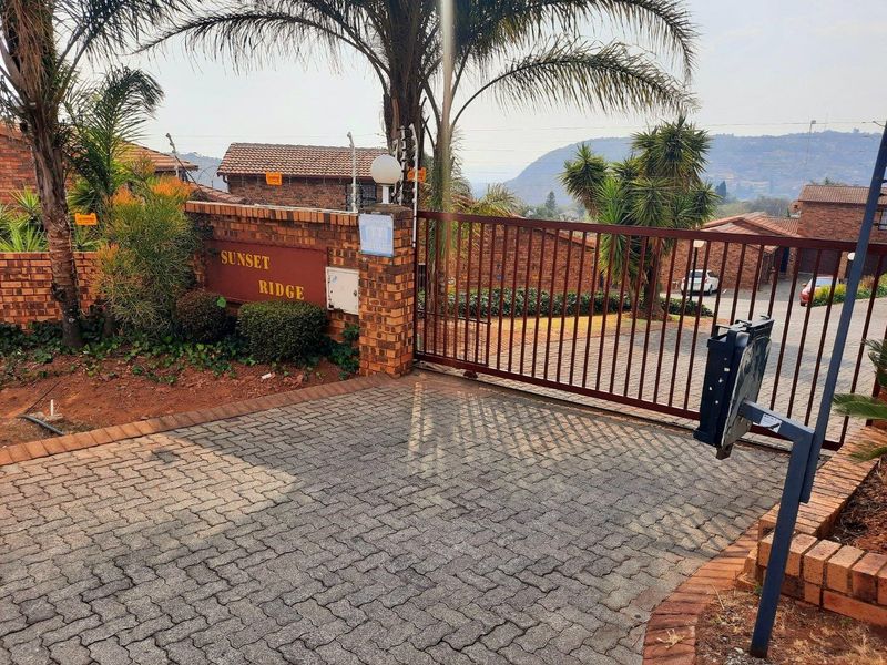Entrance to Sunset Ridge townhouse complex featuring a brick boundary wall, electric fencing, and a sliding security gate with paved driveway access.