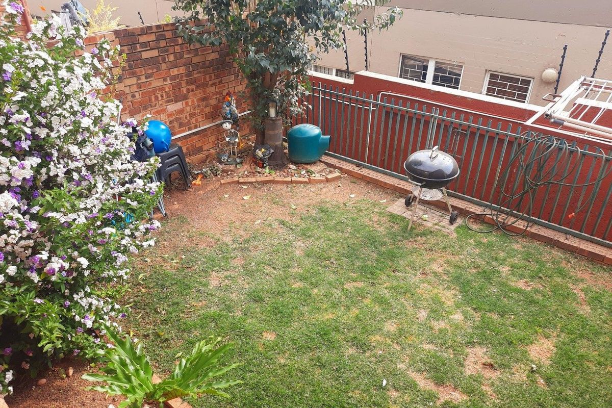 A private rear garden area featuring a brick boundary wall, metal security fencing with electric wiring, and a small lawn space.