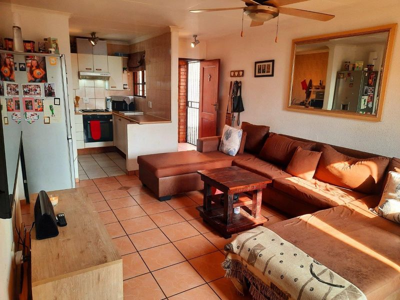 Open-plan living area featuring tiled flooring, a ceiling fan, and a compact kitchen with built-in cabinetry, oven, and hob.