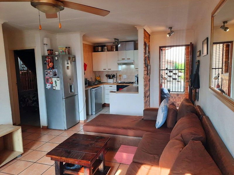 Open-plan living area featuring tiled floors, an exposed brick accent wall, and a compact kitchen with built-in cabinetry and appliances.