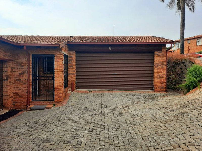 Exterior view of a townhouse garage featuring a roller shutter door, brick facade, and a paved driveway.