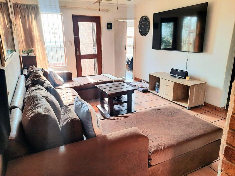 A living room featuring tiled flooring, a ceiling fan, and direct access to an exterior area through a secure door.