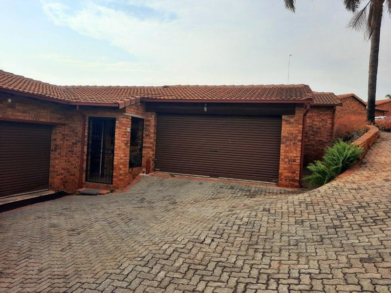 Front exterior view of a townhouse featuring a brick facade, tiled roof, and a paved driveway leading to a roller garage door.