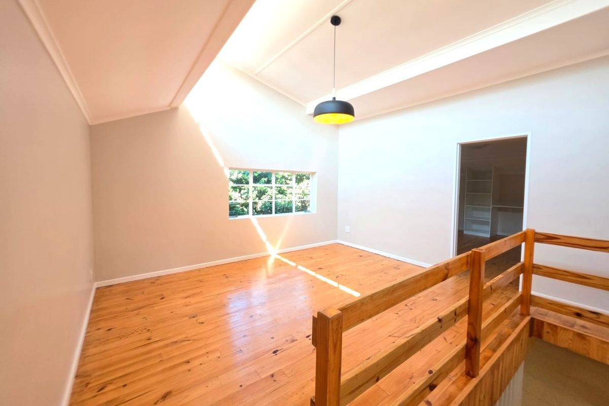 A bright, open-plan living area featuring polished timber flooring, a vaulted ceiling, and a timber balustrade overlooking the lower level.