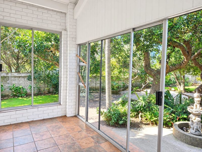 A bright, enclosed patio featuring large sliding glass doors, tiled flooring, and painted brick walls, offering a seamless transition to the garden.