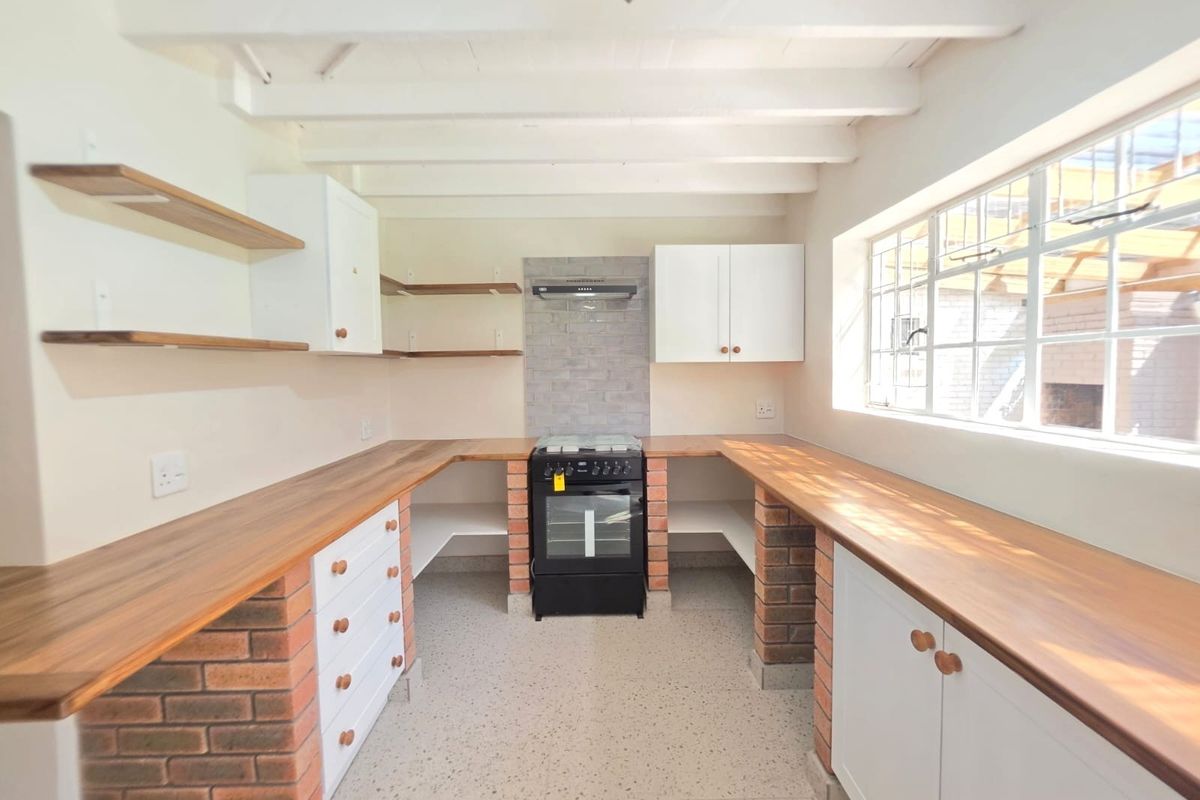 A bright, modern kitchen featuring exposed timber ceiling beams, brick-based cabinetry with wooden countertops, a freestanding stove, and durable terrazzo flooring.
