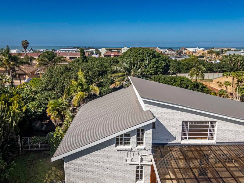 Aerial view of the property featuring a painted brick exterior, metal roofing, and a covered patio area, set within a coastal neighborhood.