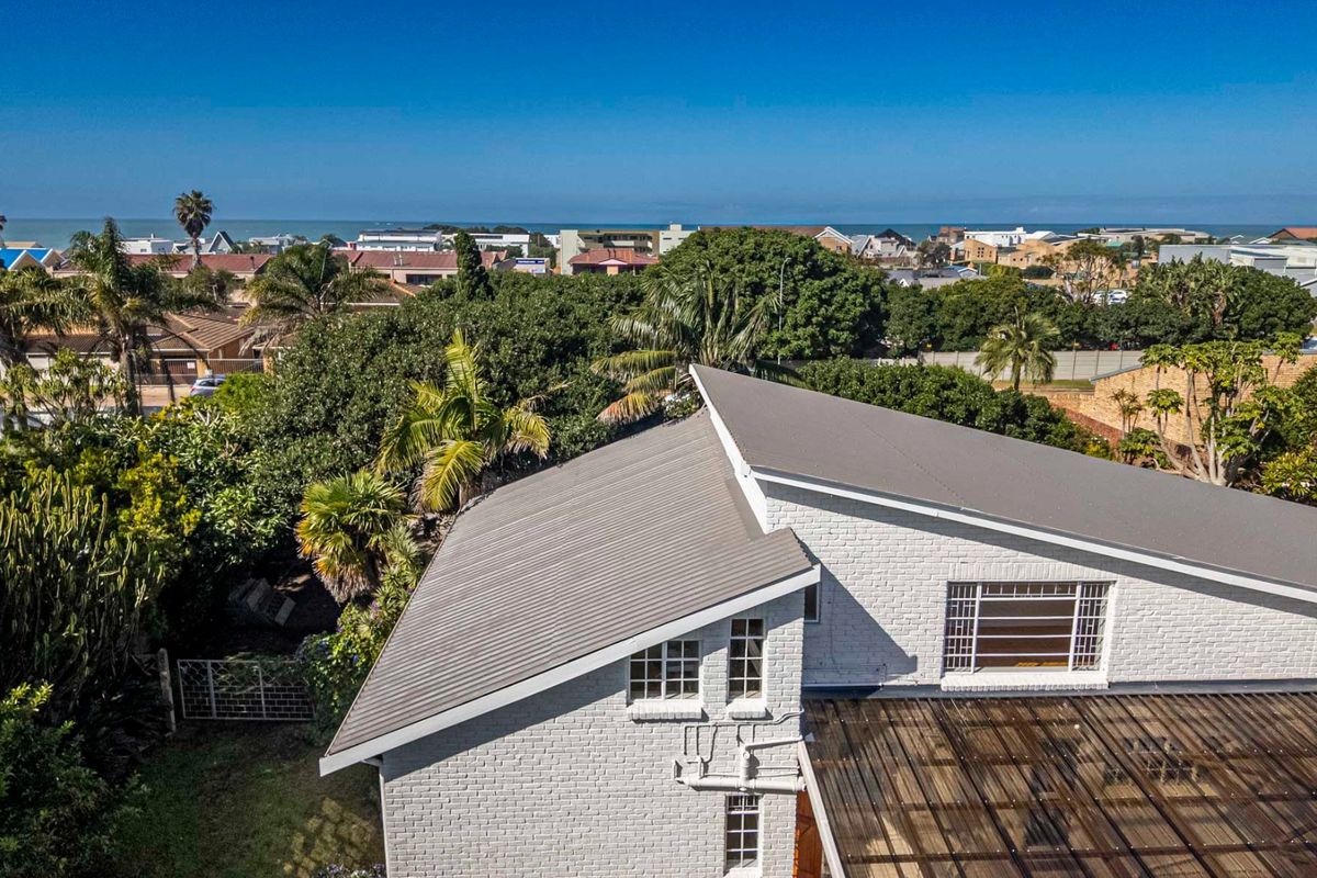 Aerial view of the property featuring a painted brick exterior, metal roofing, and a covered patio area, set within a coastal neighborhood.