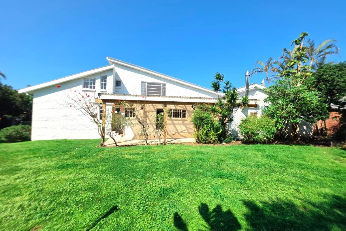 Rear view of the property featuring a white brick facade, a timber pergola, and a well-maintained garden lawn.