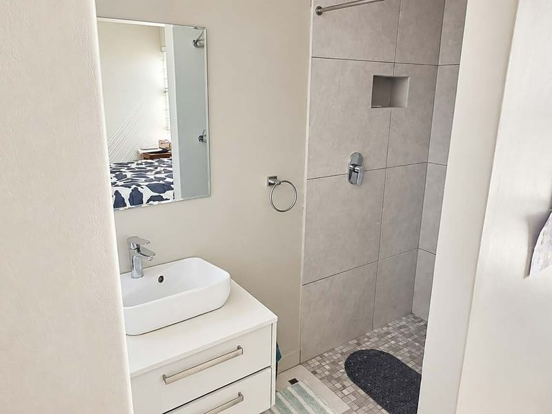 Modern bathroom featuring a white vanity with a vessel sink, a tiled shower enclosure with a recessed niche, and a wall-mounted mirror.
