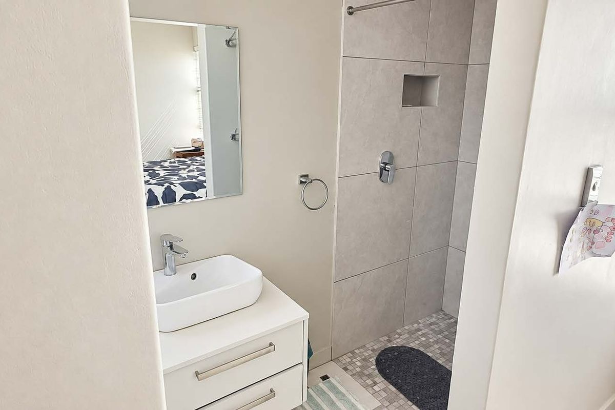 Modern bathroom featuring a white vanity with a vessel sink, a tiled shower enclosure with a recessed niche, and a wall-mounted mirror.
