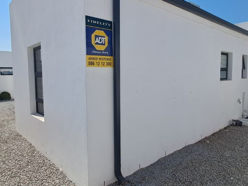 A view of the rear exterior of the property featuring white rendered walls, gravel landscaping, and a security alarm system sign.