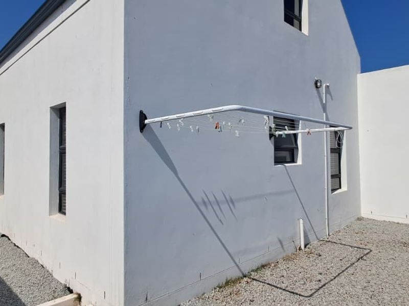 Rear exterior view of the property featuring white rendered walls, gravel landscaping, and a wall-mounted clothesline.
