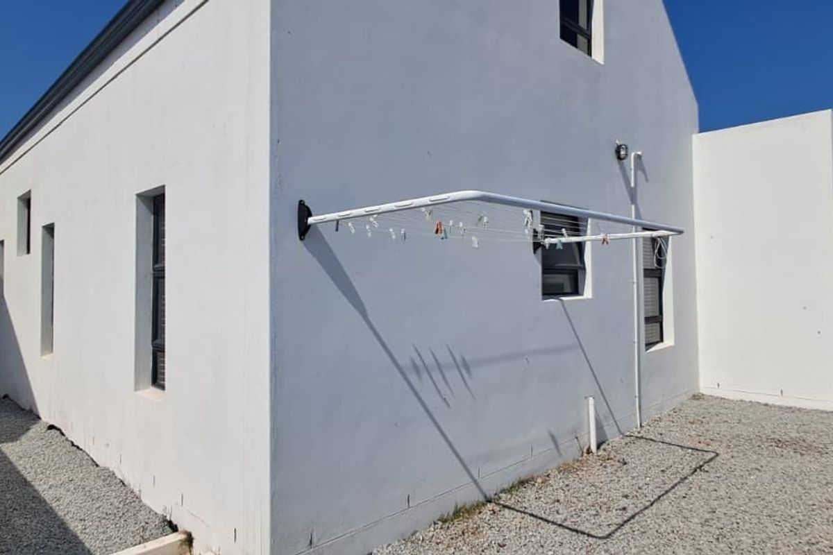 Rear exterior view of the property featuring white rendered walls, gravel landscaping, and a wall-mounted clothesline.