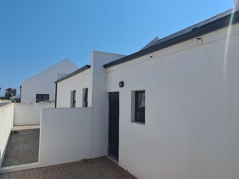 A view of the rear exterior of the property featuring a paved courtyard, gravel garden area, and secure boundary walls.