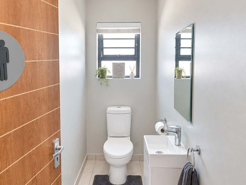 A compact, modern guest bathroom featuring a white toilet, wall-mounted basin with mixer tap, and a mirror, finished with clean neutral walls.