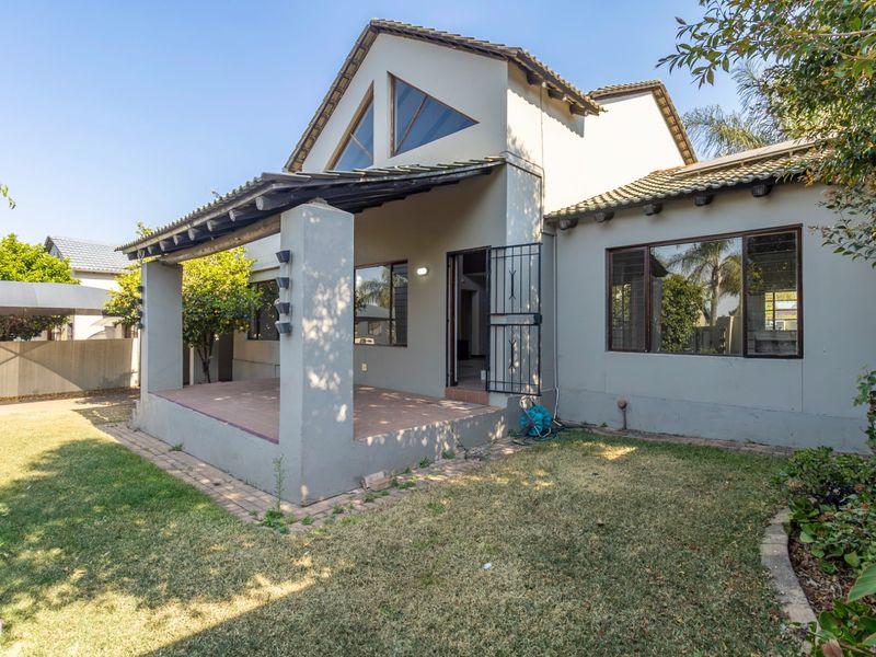 Rear view of the house featuring a covered patio, tiled roof, and large triangular windows overlooking a private garden area.