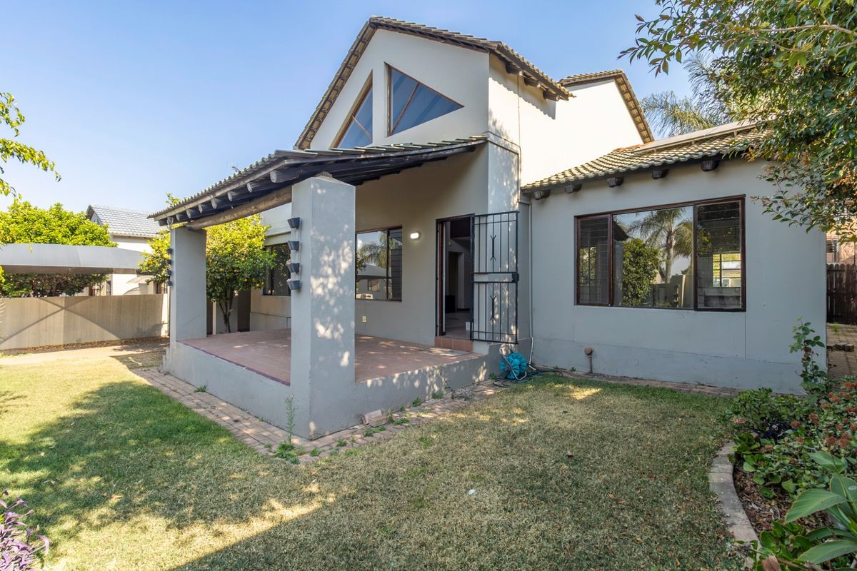 Rear view of the house featuring a covered patio, tiled roof, and large triangular windows overlooking a private garden area.