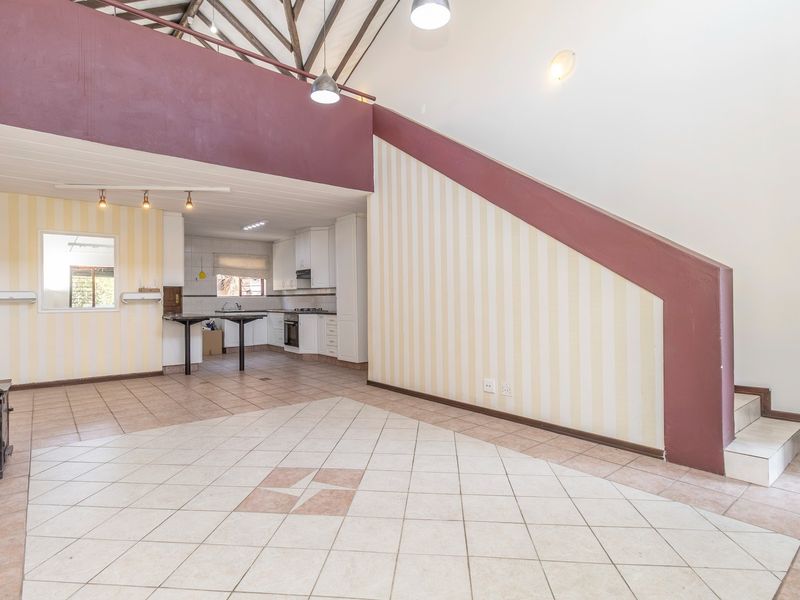 Spacious open-plan living and kitchen area featuring vaulted ceilings with exposed beams, tiled flooring, and a built-in wood-burning stove.